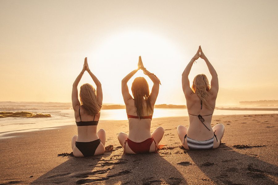 Three friends in sun salutation on the beach at sunrise