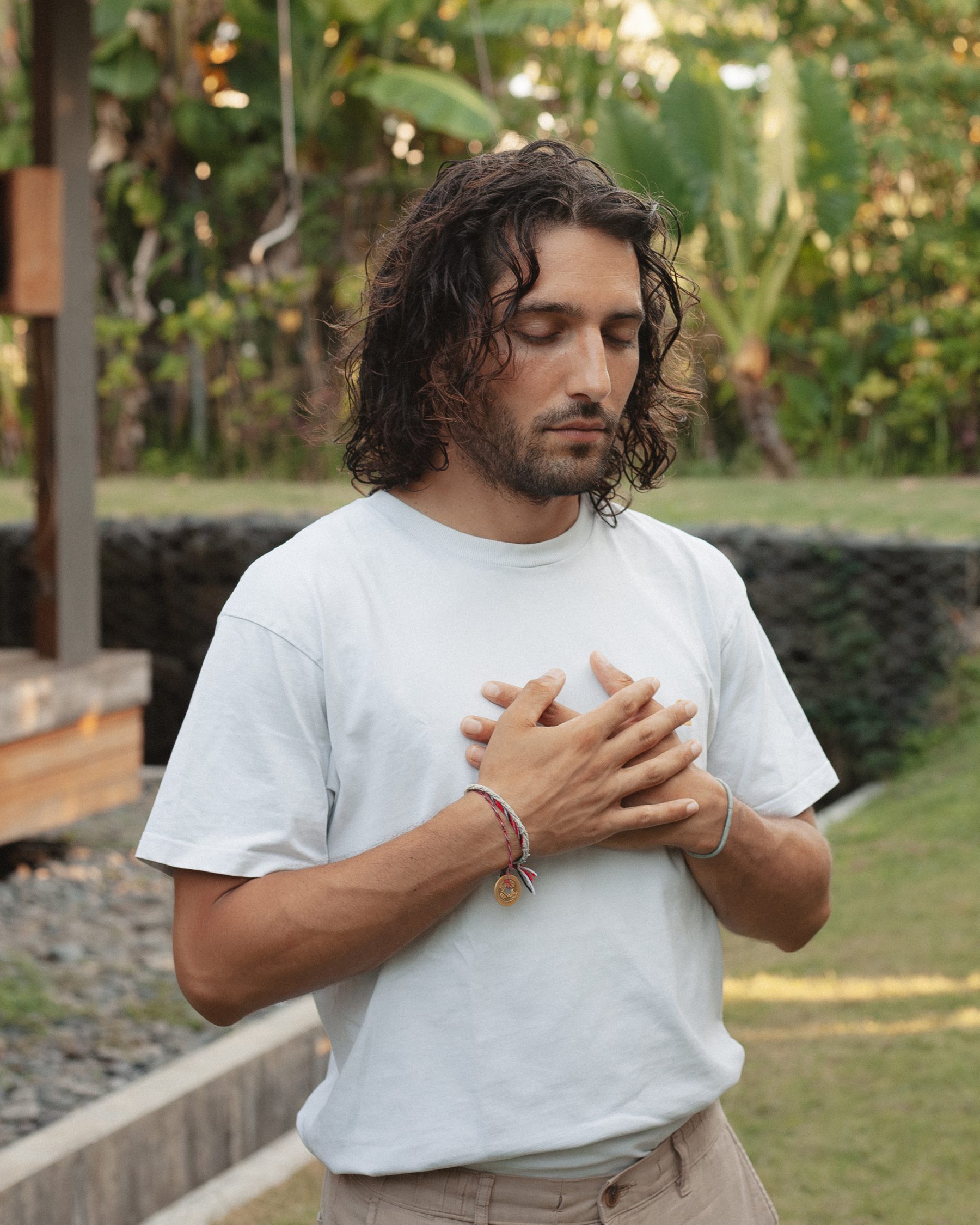 A Samasti graduate standing in the garden with both hands on his chest, eyes closed