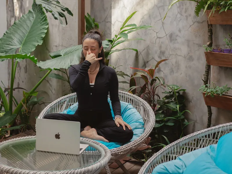 A student practising alternate nostril breathing at home with a laptop open beside her